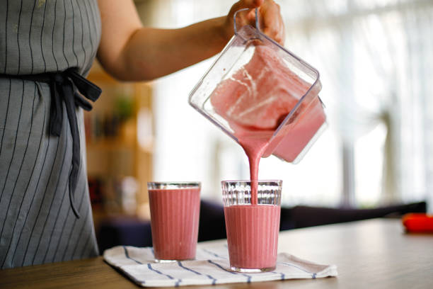 Young woman pouring strawberry milkshake from blender
