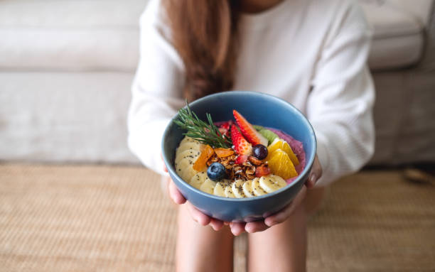 A woman holding healthy blueberry smoothie bowl with mixed fruits topping